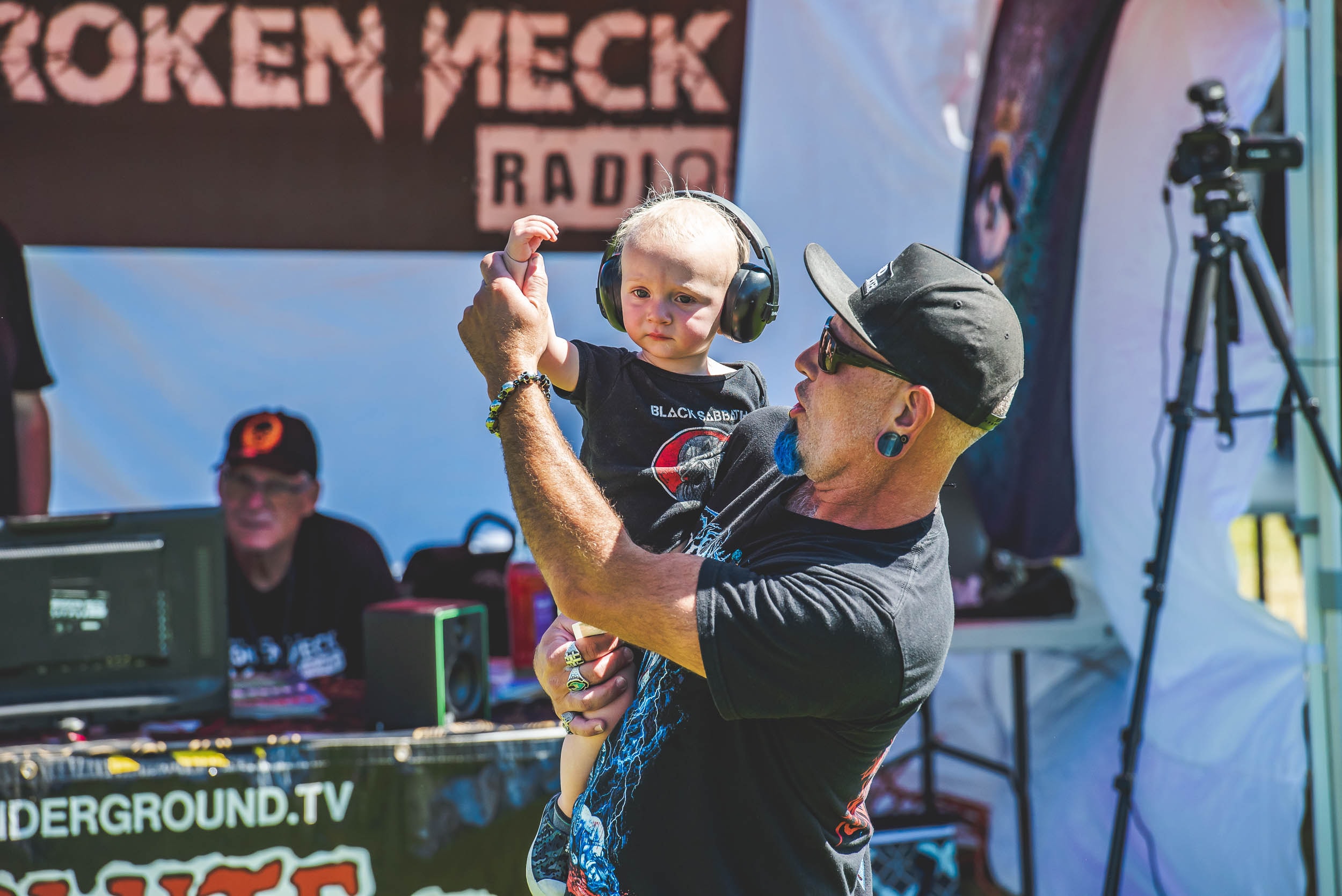 Baby wearing headphones held up by dad near the Broken Neck Radio stage
