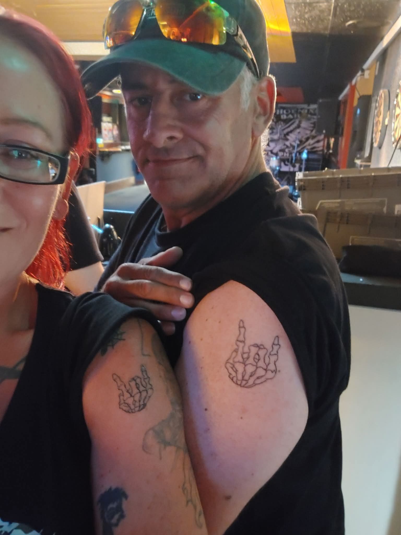 Two fans showing off matching skeleton horns tattoos at Mosh the Rock